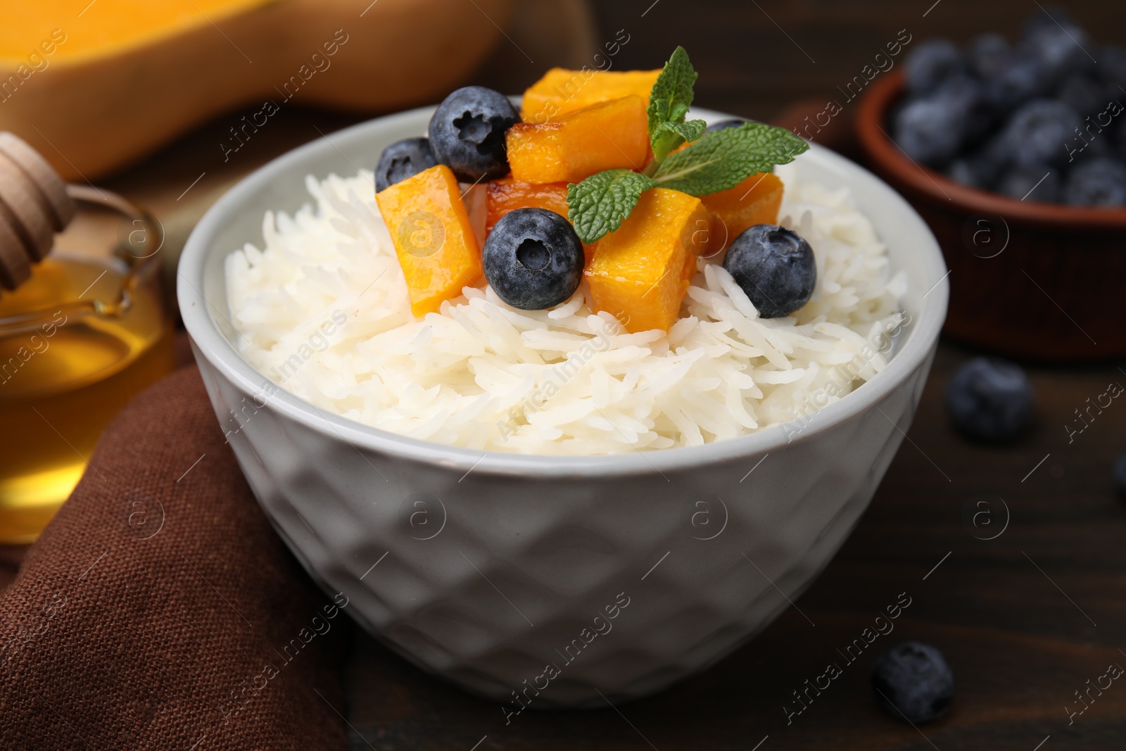 Photo of Bowl of delicious rice porridge with blueberries and pumpkin on wooden table, closeup