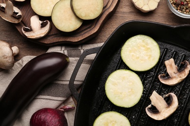 Grill pan and fresh vegetables on wooden table, flat lay