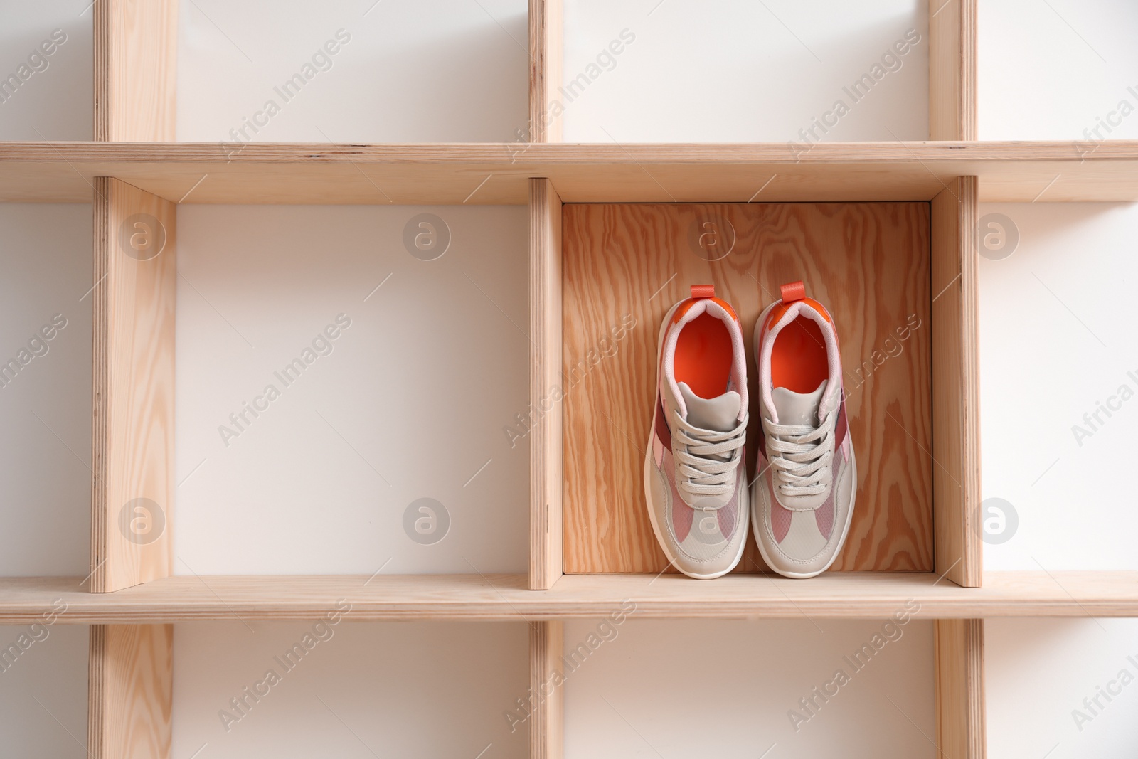 Photo of Wooden shelving unit with stylish women's sneakers on white wall