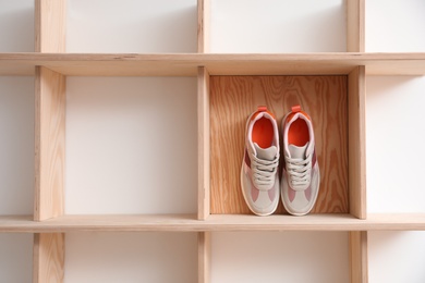 Photo of Wooden shelving unit with stylish women's sneakers on white wall