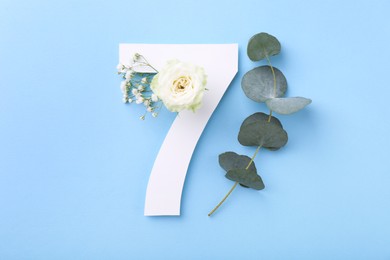 Photo of Paper number 7, beautiful flowers and eucalyptus branch on light blue background, top view