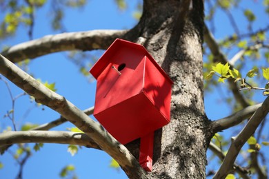 Photo of Red bird house on tree trunk outdoors, low angle view