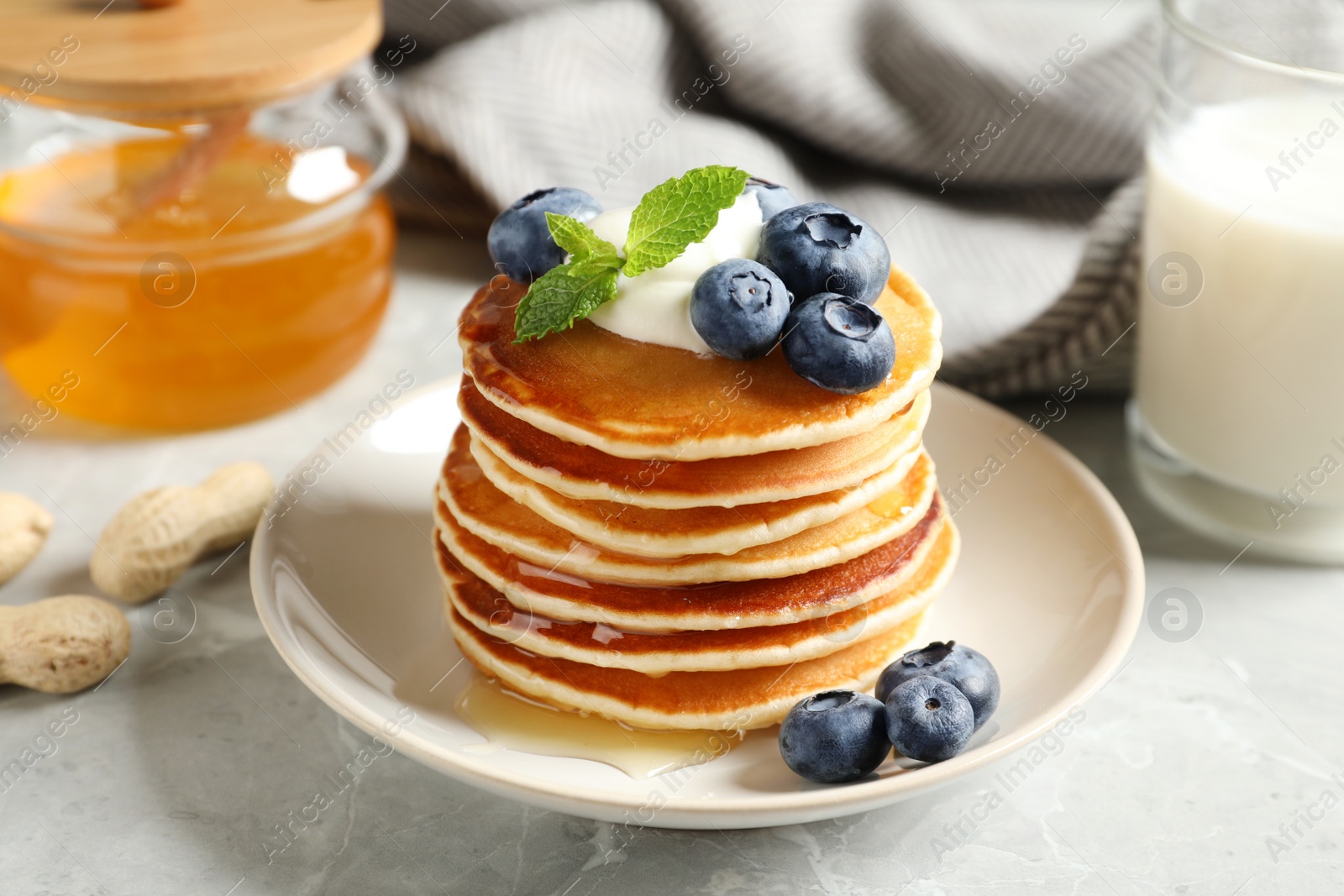 Photo of Plate of tasty pancakes with blueberries, sauce and mint on grey marble table