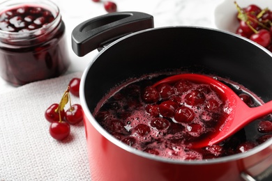 Photo of Pot with cherries in sugar syrup on table, closeup. Making delicious jam