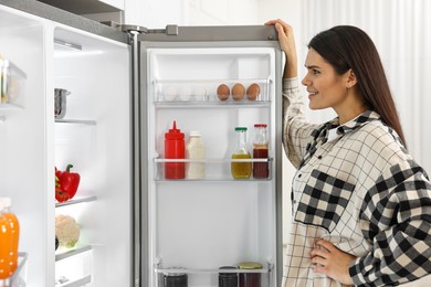 Young woman near modern refrigerator in kitchen