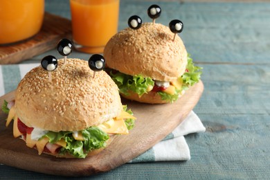 Photo of Cute monster burgers served on blue wooden table. Halloween party food