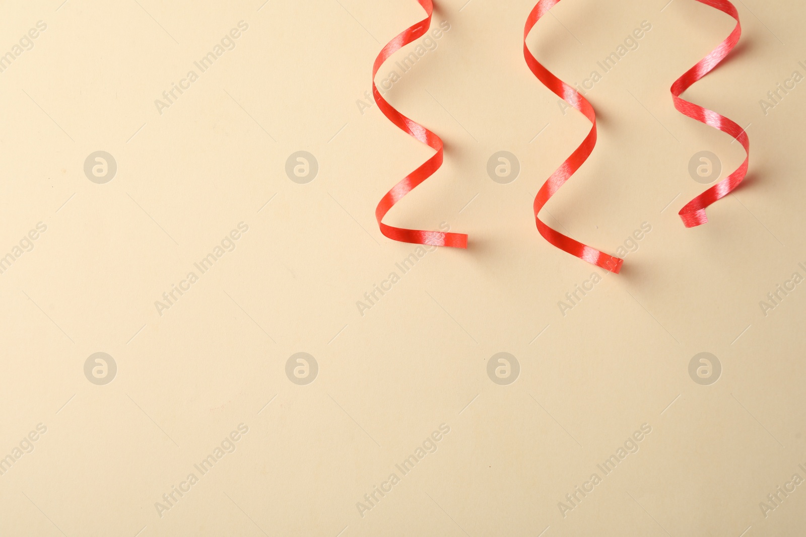 Photo of Shiny red serpentine streamers on beige background, flat lay. Space for text