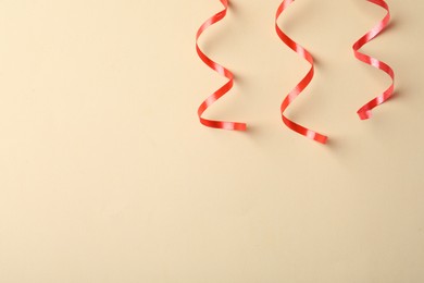 Photo of Shiny red serpentine streamers on beige background, flat lay. Space for text