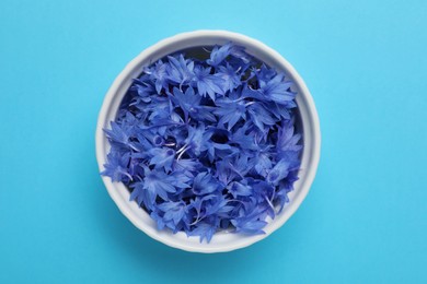 Beautiful bright cornflowers petals in bowl on light blue background, top view