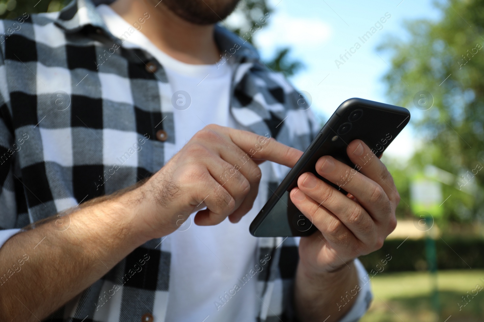 Photo of Young man with smartphone in park on summer day, closeup