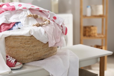 Laundry basket with baby clothes on white table indoors