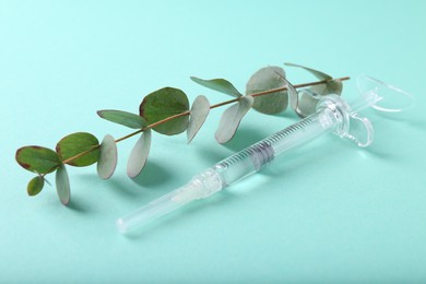 Photo of Cosmetology. Medical syringe and eucalyptus branch on turquoise background, closeup