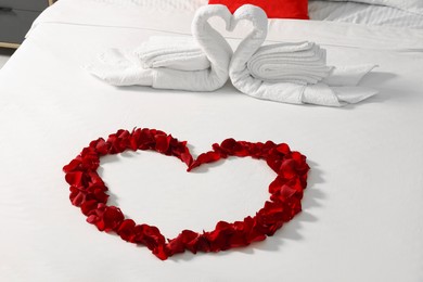 Photo of Honeymoon. Swans made with towels and heart of beautiful rose petals on bed in room