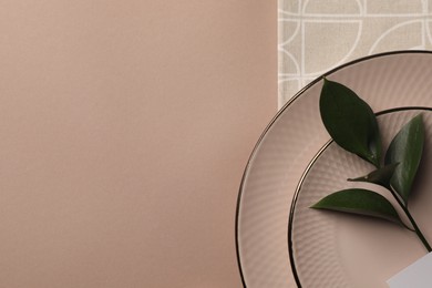 Napkin, plates and green twig on beige table, top view. Space for text