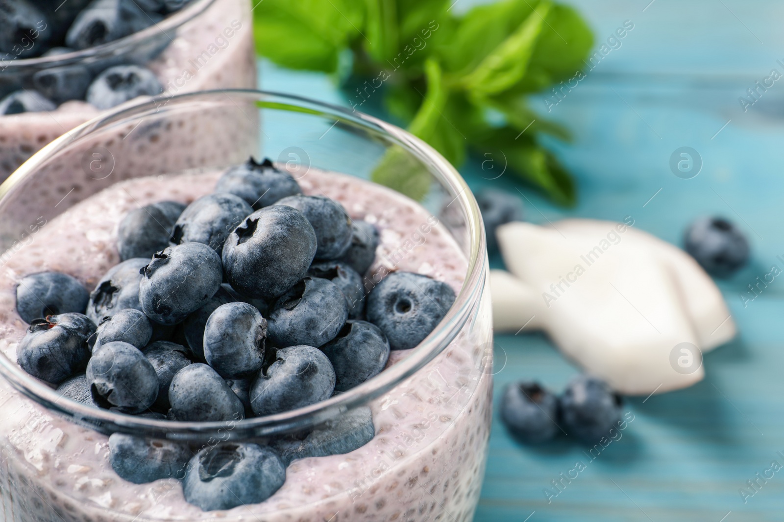 Photo of Delicious chia pudding with blueberries in glass on light blue table, closeup. Space for text