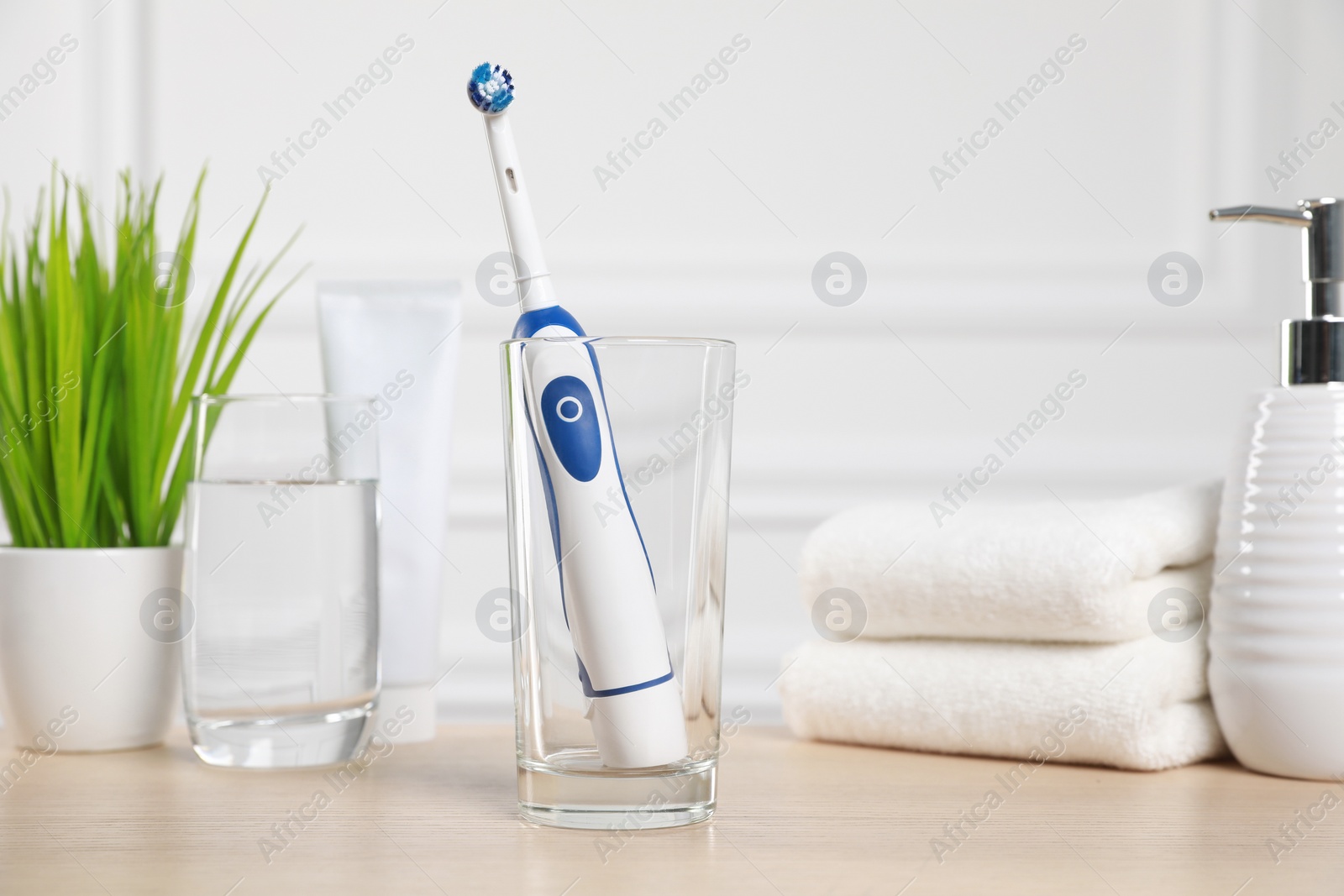 Photo of Electric toothbrush, glass of water and toiletries on wooden table