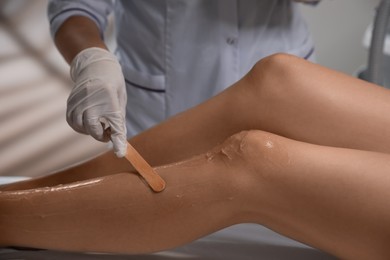 Photo of Professional cosmetologist applying gel on client's leg before laser epilation procedure in salon, closeup