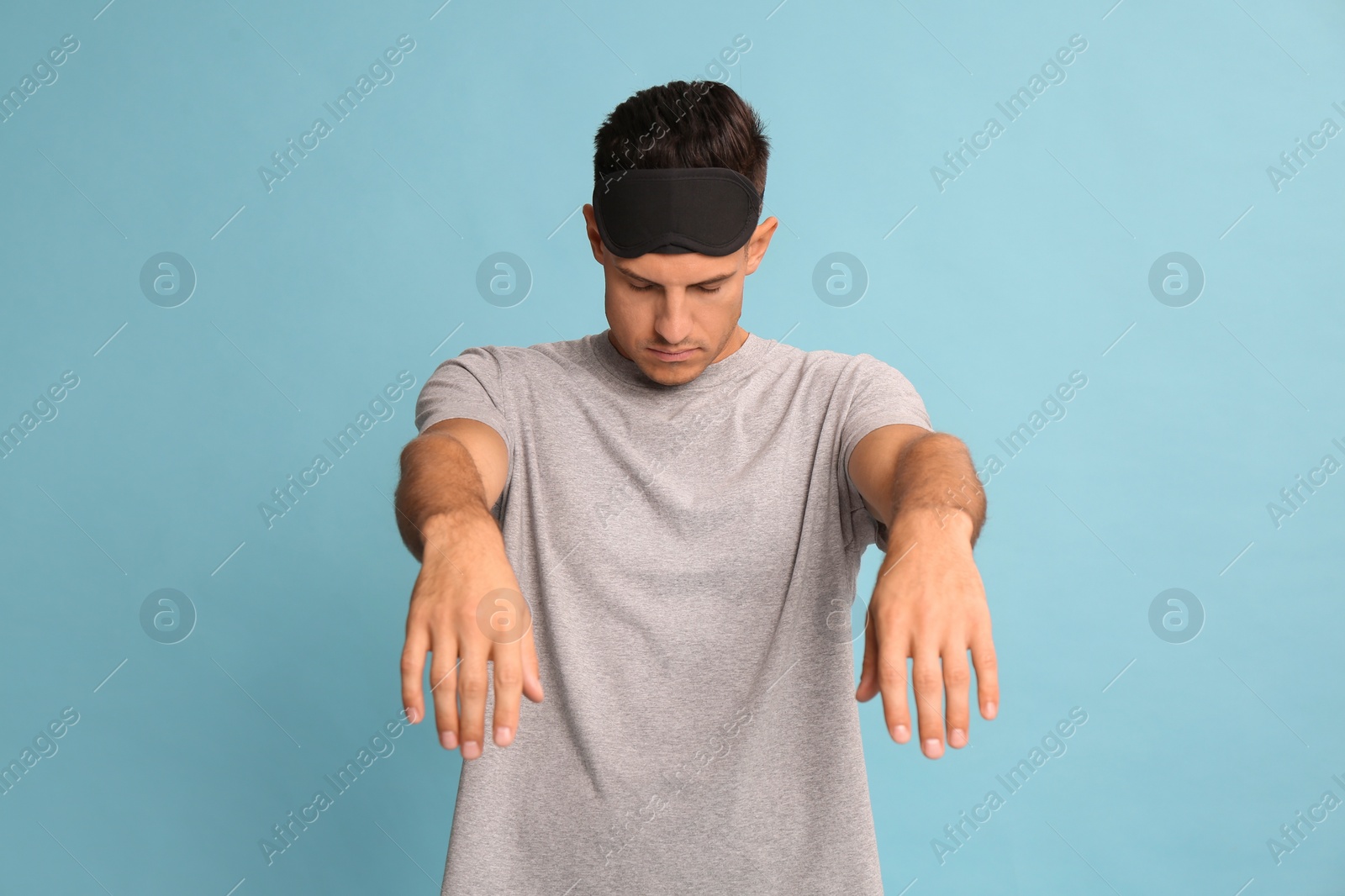 Photo of Somnambulist with blindfold on light blue background. Sleepwalking