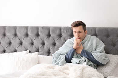 Sick young man with cough suffering from cold in bed