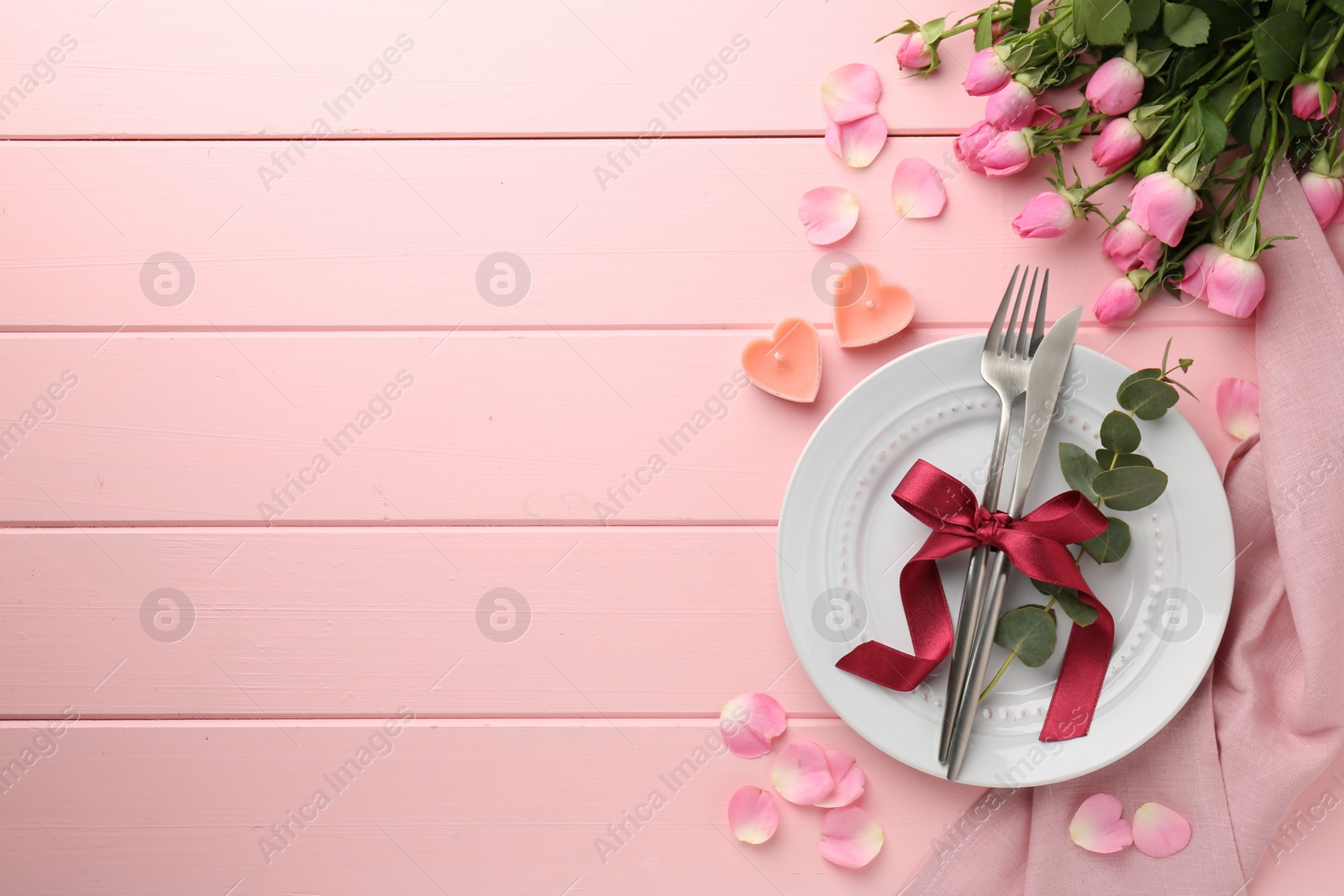 Photo of Place setting with heart shaped candles and bouquet of roses for romantic dinner on pink wooden table, flat lay. Space for text