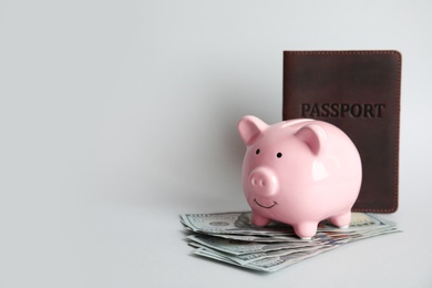 Photo of Piggy bank with passport and money on light background, space for text. Travel agency