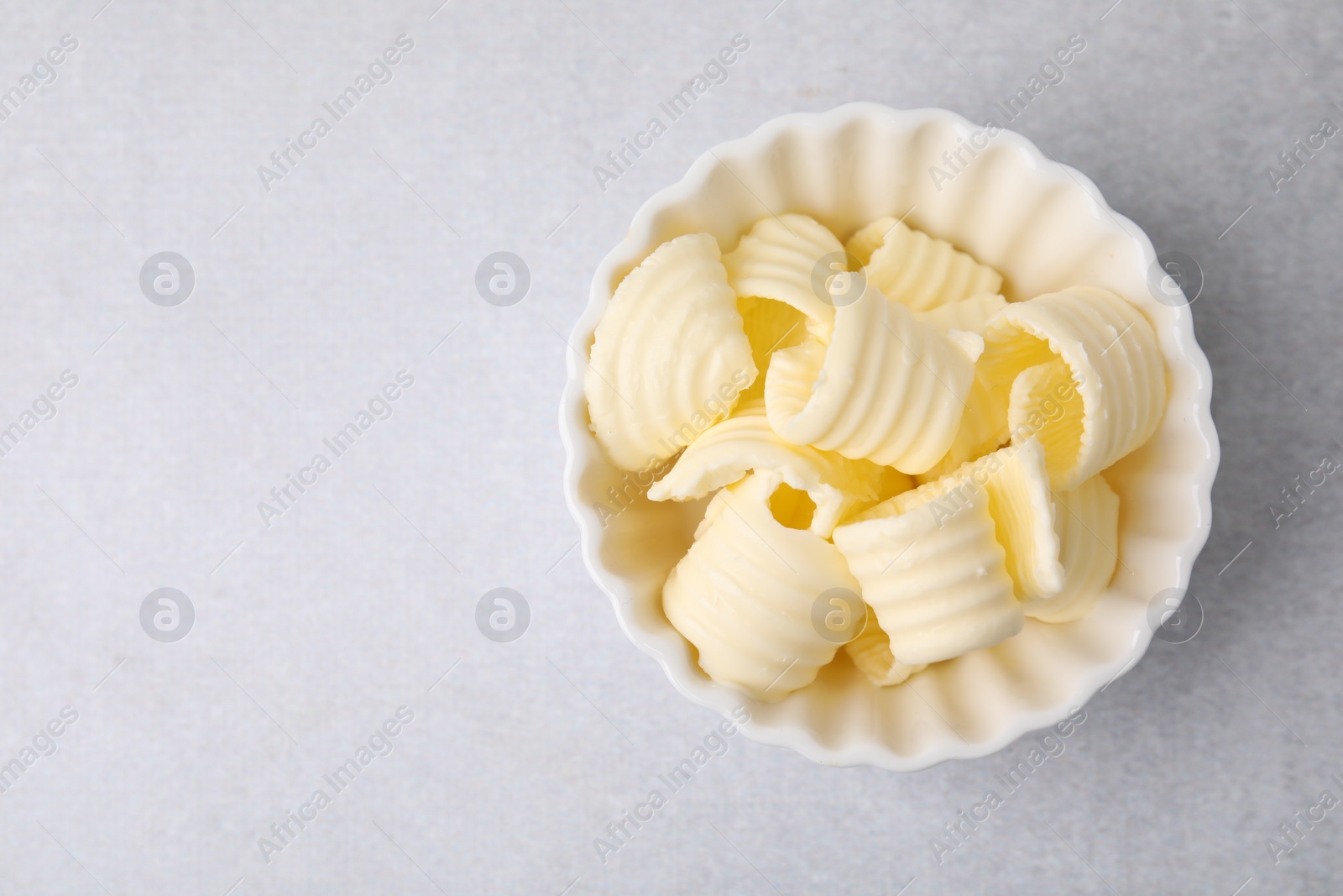 Photo of Tasty butter curls in bowl on light grey table, top view. Space for text