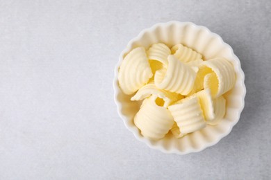 Photo of Tasty butter curls in bowl on light grey table, top view. Space for text