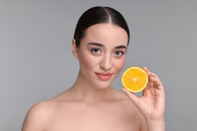 Photo of Beautiful young woman with piece of orange on grey background