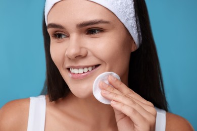 Young woman with cotton pad on light blue background, closeup