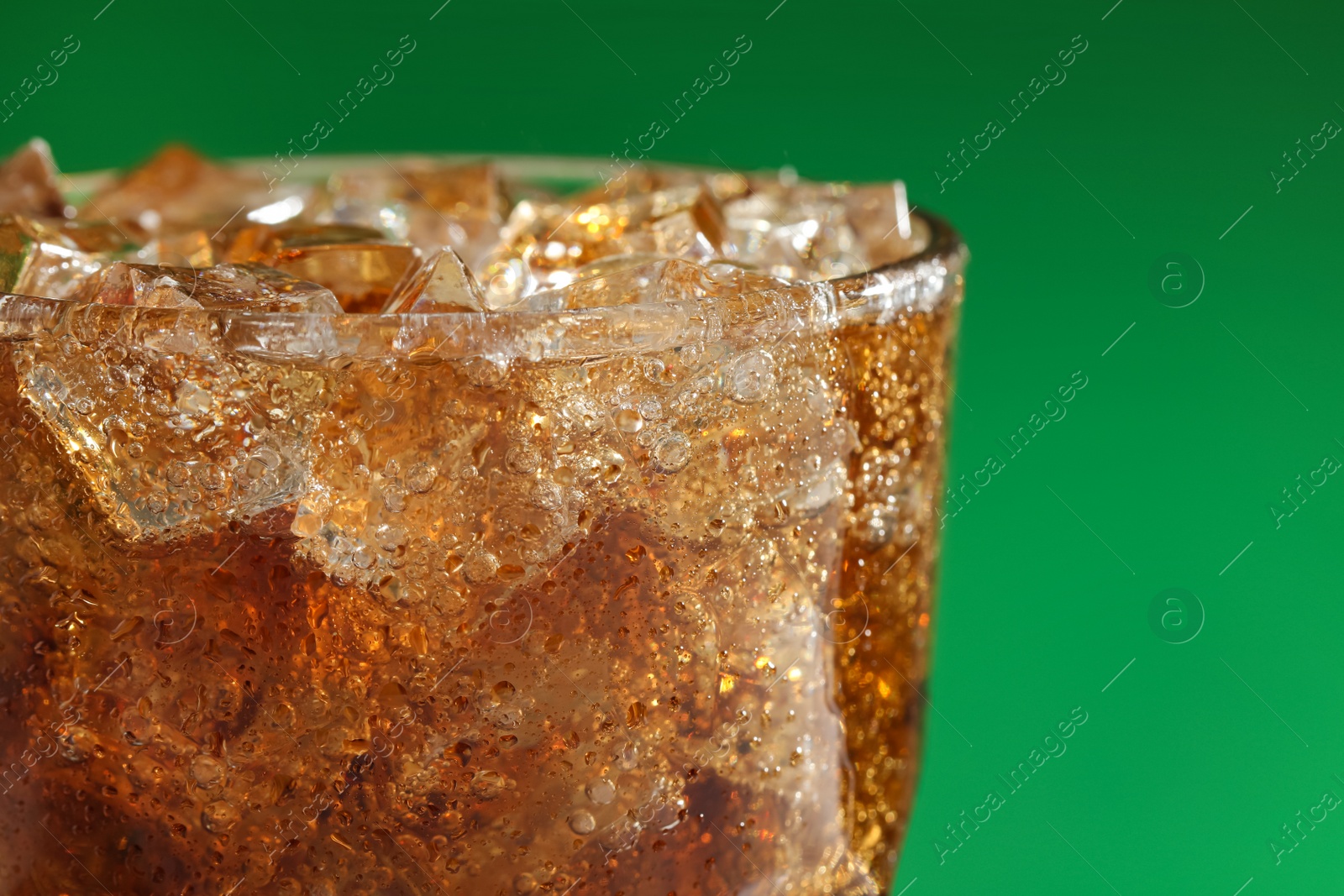 Photo of Glass of refreshing soda drink with ice cubes on green background, closeup