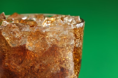 Glass of refreshing soda drink with ice cubes on green background, closeup