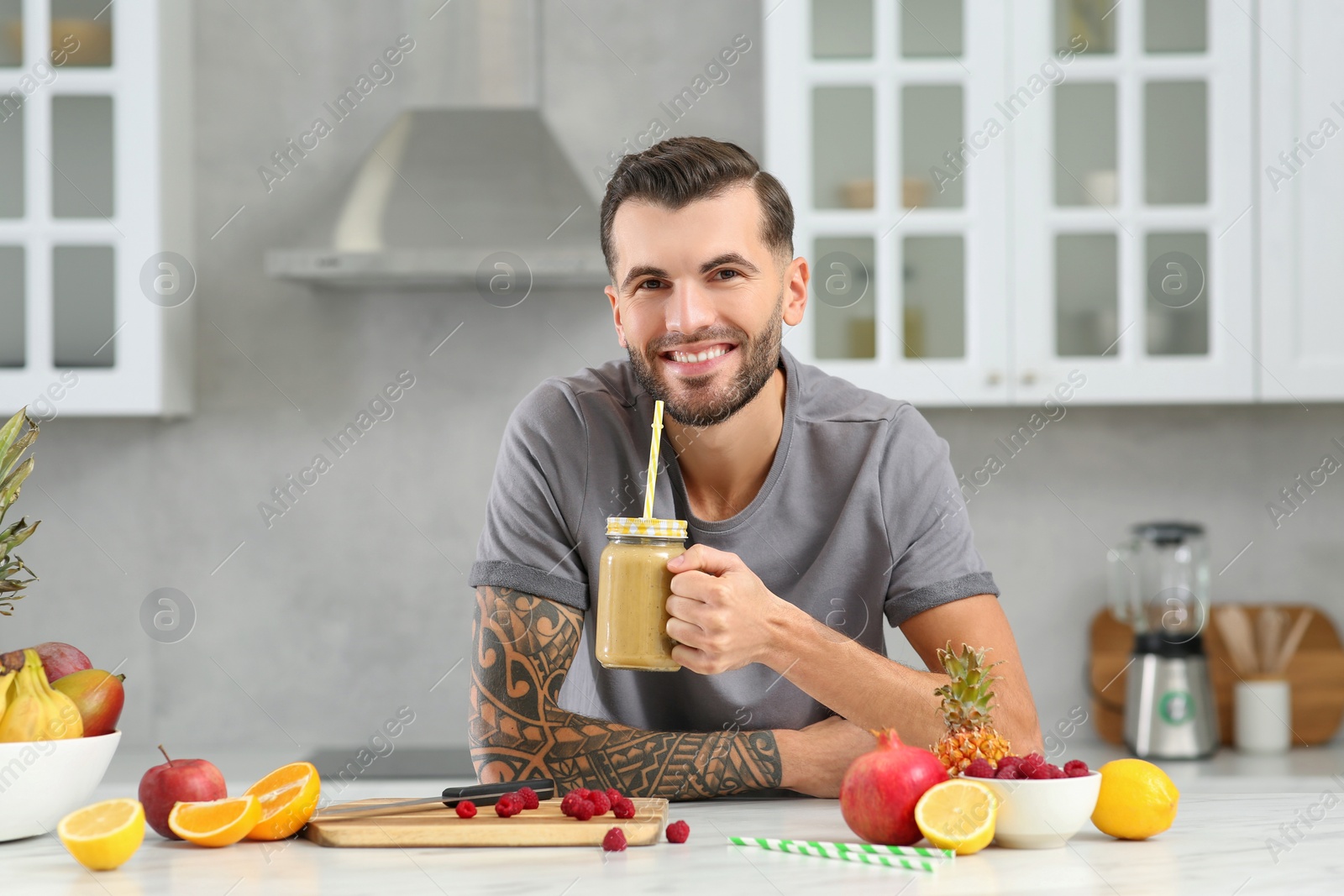 Photo of Handsome man with delicious smoothie at white table in kitchen