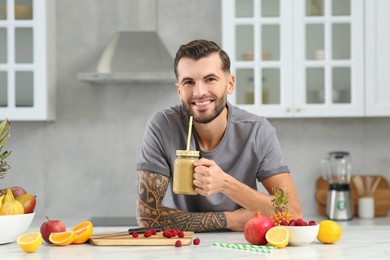 Photo of Handsome man with delicious smoothie at white table in kitchen