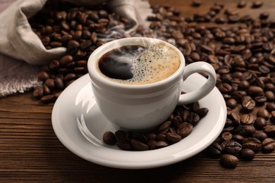 Cup of aromatic hot coffee and beans on wooden table