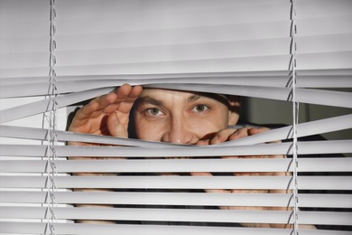 Curious man looking through Venetian window blinds