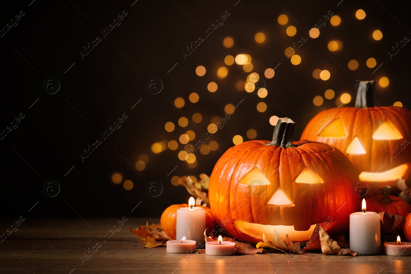 Photo of Pumpkin jack o'lanterns, autumn leaves and candles on table against blurred background, space for text. Halloween decor