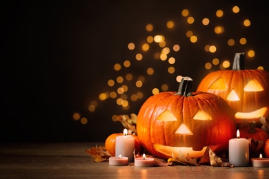 Photo of Pumpkin jack o'lanterns, autumn leaves and candles on table against blurred background, space for text. Halloween decor