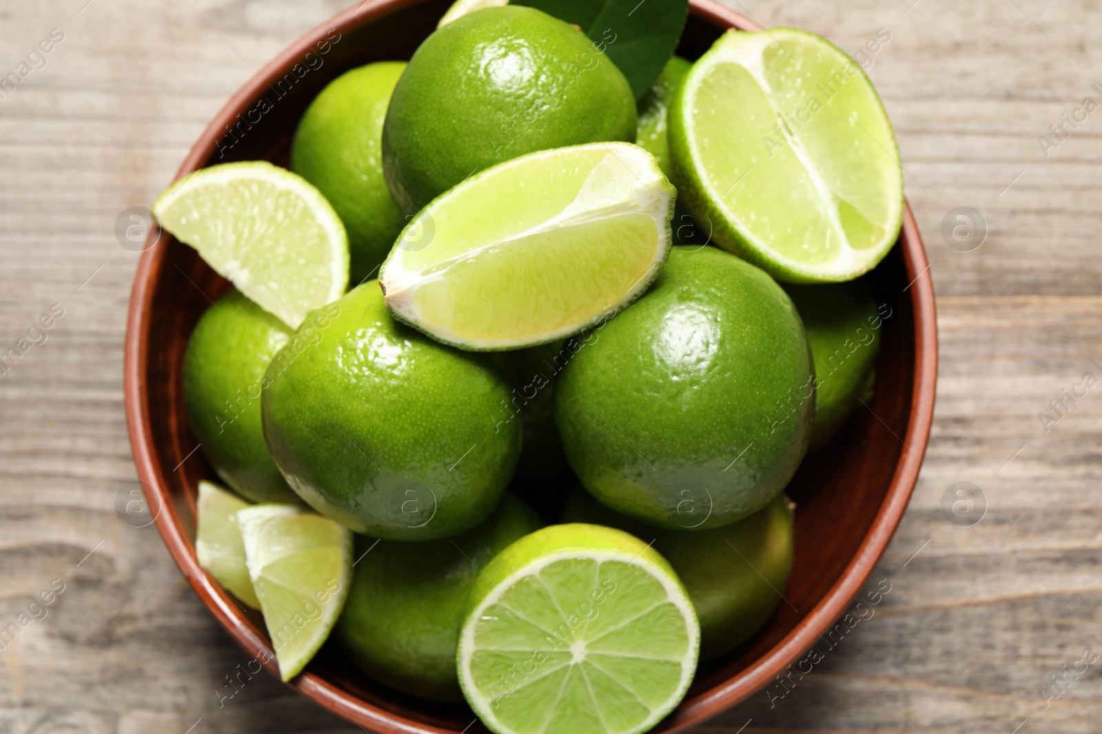 Photo of Tasty ripe limes in bowl on wooden table, top view