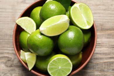 Tasty ripe limes in bowl on wooden table, top view