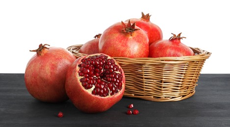 Fresh pomegranates in wicker basket on black wooden table against white background