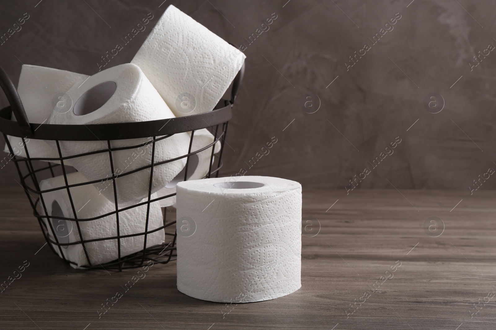 Photo of Soft toilet paper rolls in metal basket on wooden table, closeup. Space for text