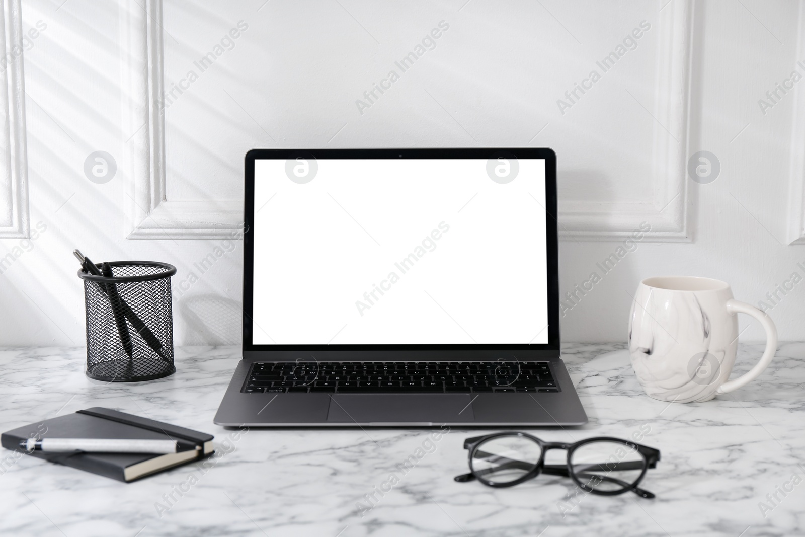 Photo of Office workplace with computer, glasses, cup and stationery on marble table near white wall