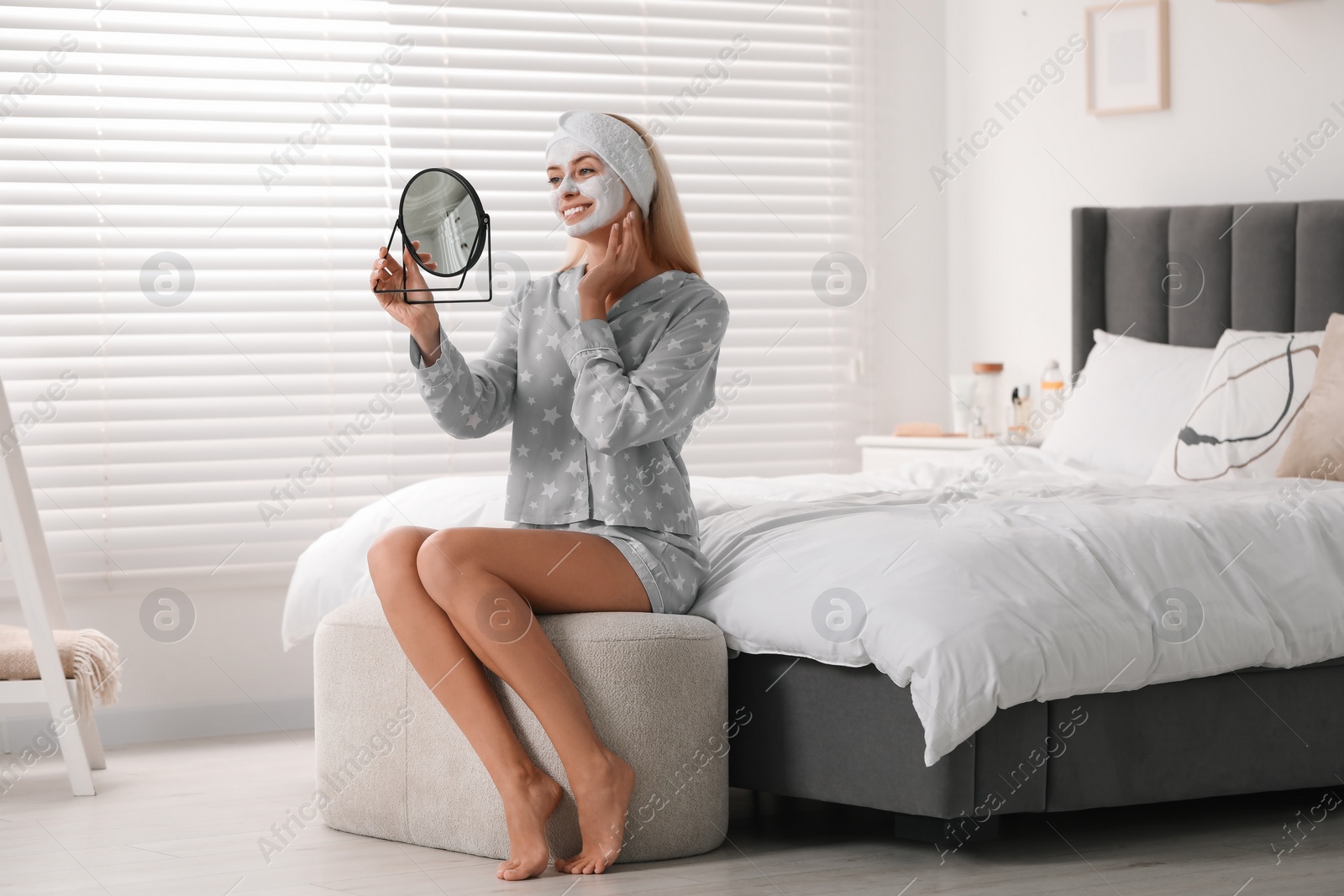 Photo of Young woman with face mask looking into mirror in bedroom. Spa treatments