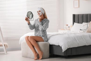 Photo of Young woman with face mask looking into mirror in bedroom. Spa treatments