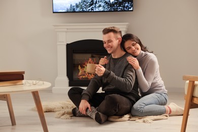 Photo of Happy lovely couple with hot drinks spending time together near fireplace at home