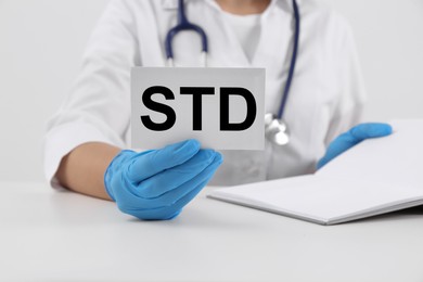 Doctor holding sheet of paper with abbreviation STD at white table, closeup