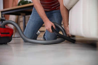 Young man using vacuum cleaner in living room, closeup