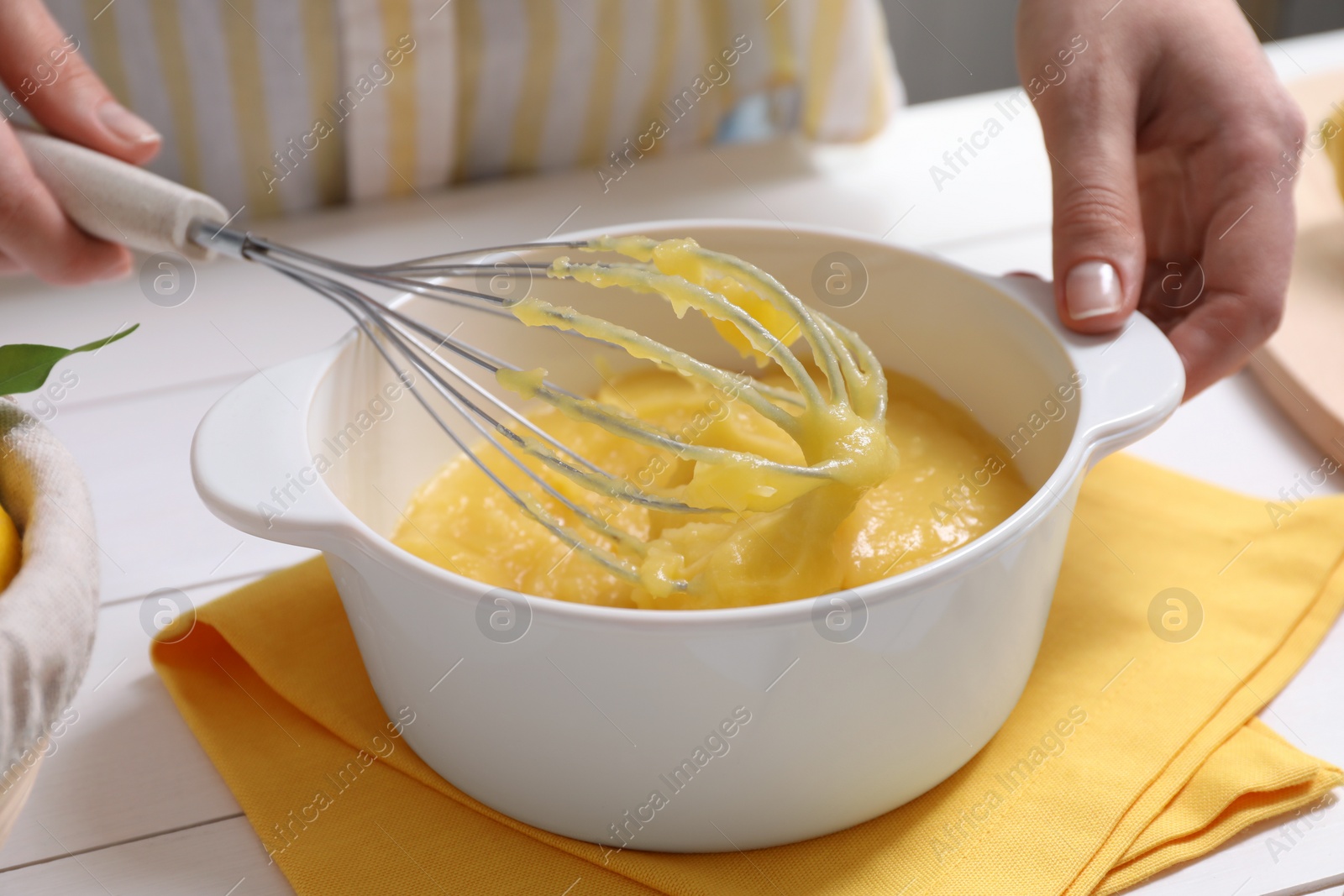 Photo of Woman cooking lemon curd at white wooden table, closeup