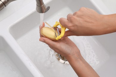 Photo of Woman peeling potato over kitchen sink with garbage disposal at home, closeup