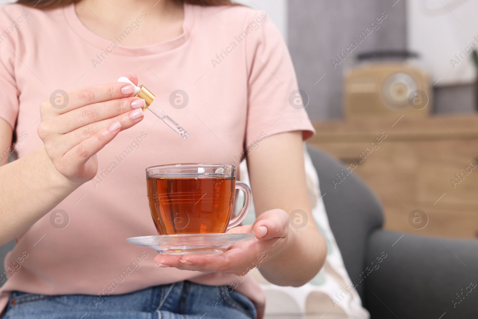 Photo of Woman dripping food supplement into cup of tea indoors, closeup